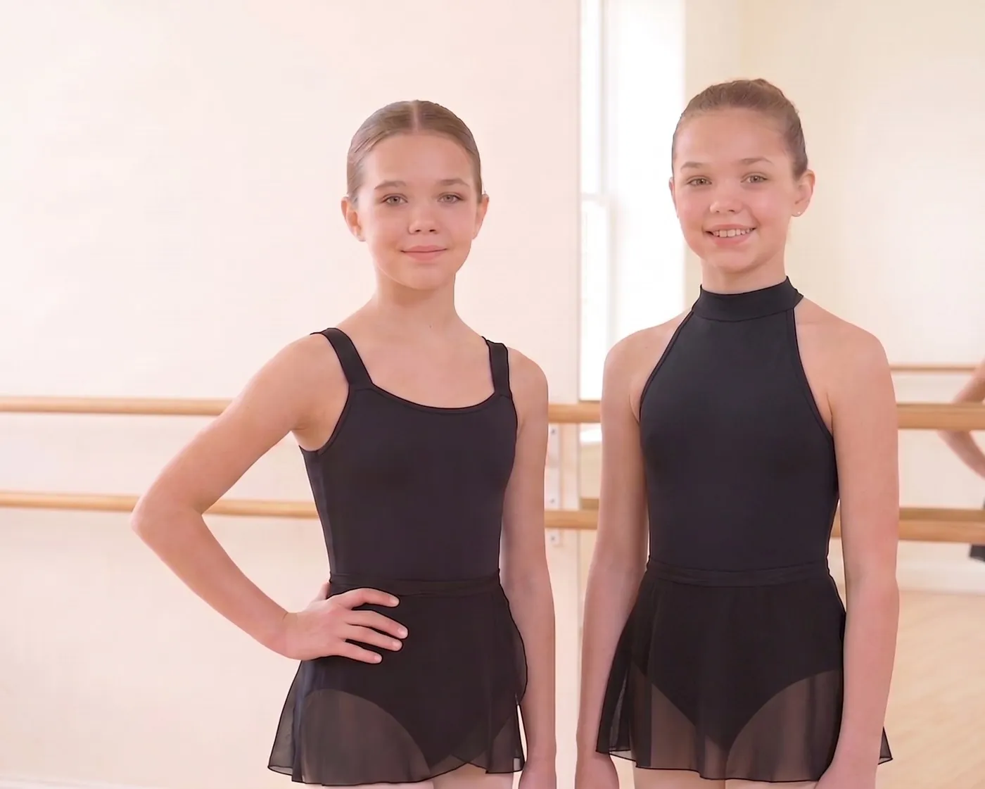Two dancers in black leotards, one wide-strap tank and one mock turtleneck